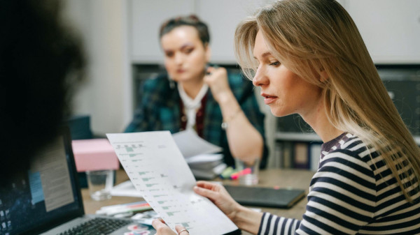 zwei-frauen-sitzen-an-einem-tisch-und-schauen-auf-ein-blatt-papier