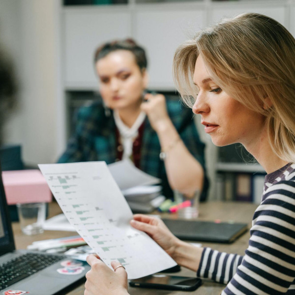 zwei-frauen-sitzen-an-einem-tisch-und-schauen-auf-ein-blatt-papier