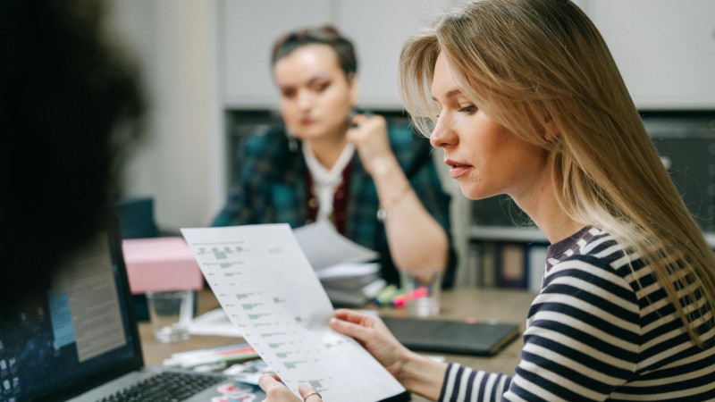 zwei-frauen-sitzen-an-einem-tisch-und-schauen-auf-ein-blatt-papier
