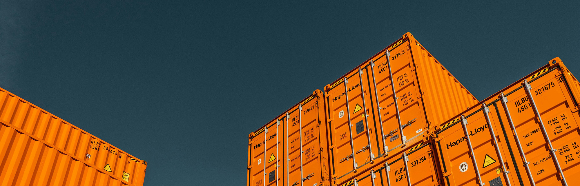 Gestapelte orangene Frachtcontainer vor blauem Himmel