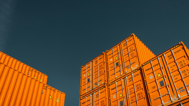 Gestapelte orangene Frachtcontainer vor blauem Himmel