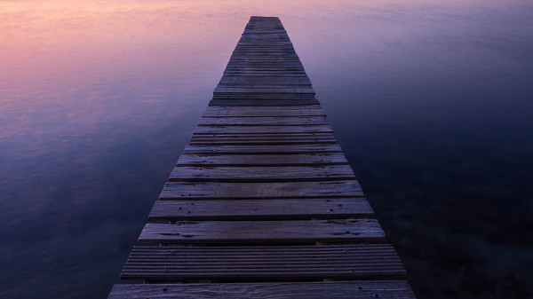 Ein alter Holzsteg, der in einen ruhigen See hineinragt und in der Ferne einen farbenfrohen Sonnenuntergang einfängt.